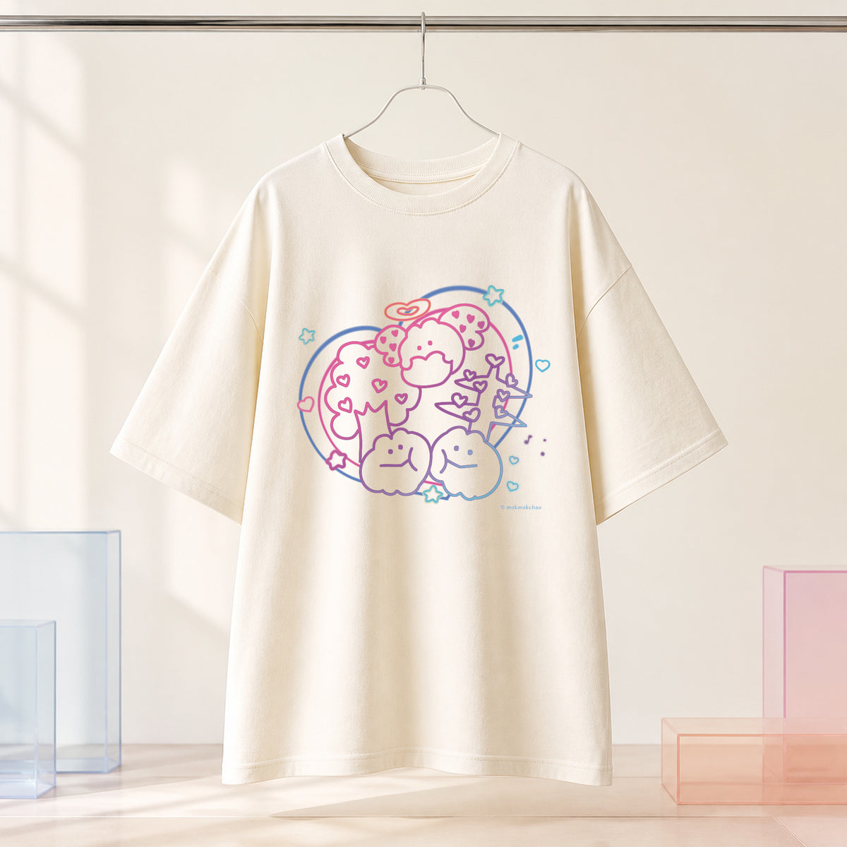 もくもくちゃんのパステル柄をプリントしたアイボリーのオーバーサイズTシャツを、ハンガーで見せた商品画像。
